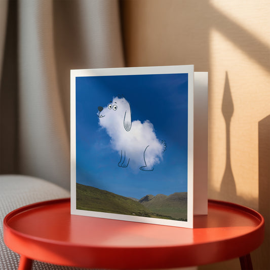 Greeting card with a cloud-shaped dog on a scenic background, placed on a red table.