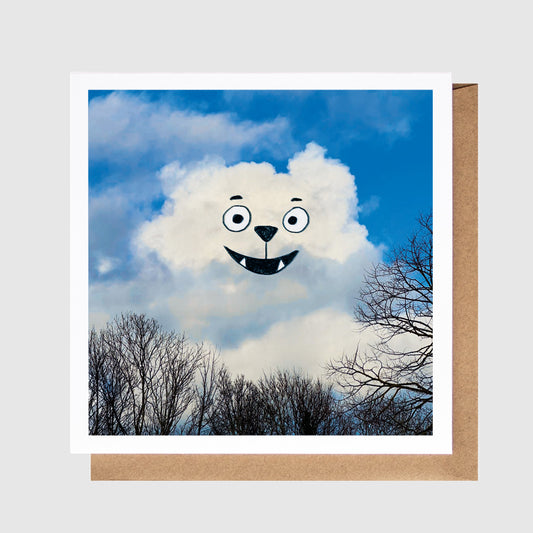 Card with a cloud shaped like a bear face against a blue sky with trees.