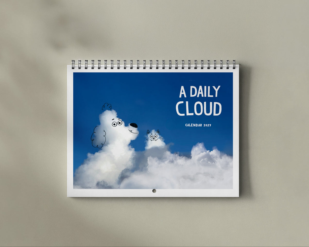 A spiral-bound desk calendar titled 'A DAILY CLOUD' hanging on a beige wall, featuring a blue sky and fluffy white clouds with faces.