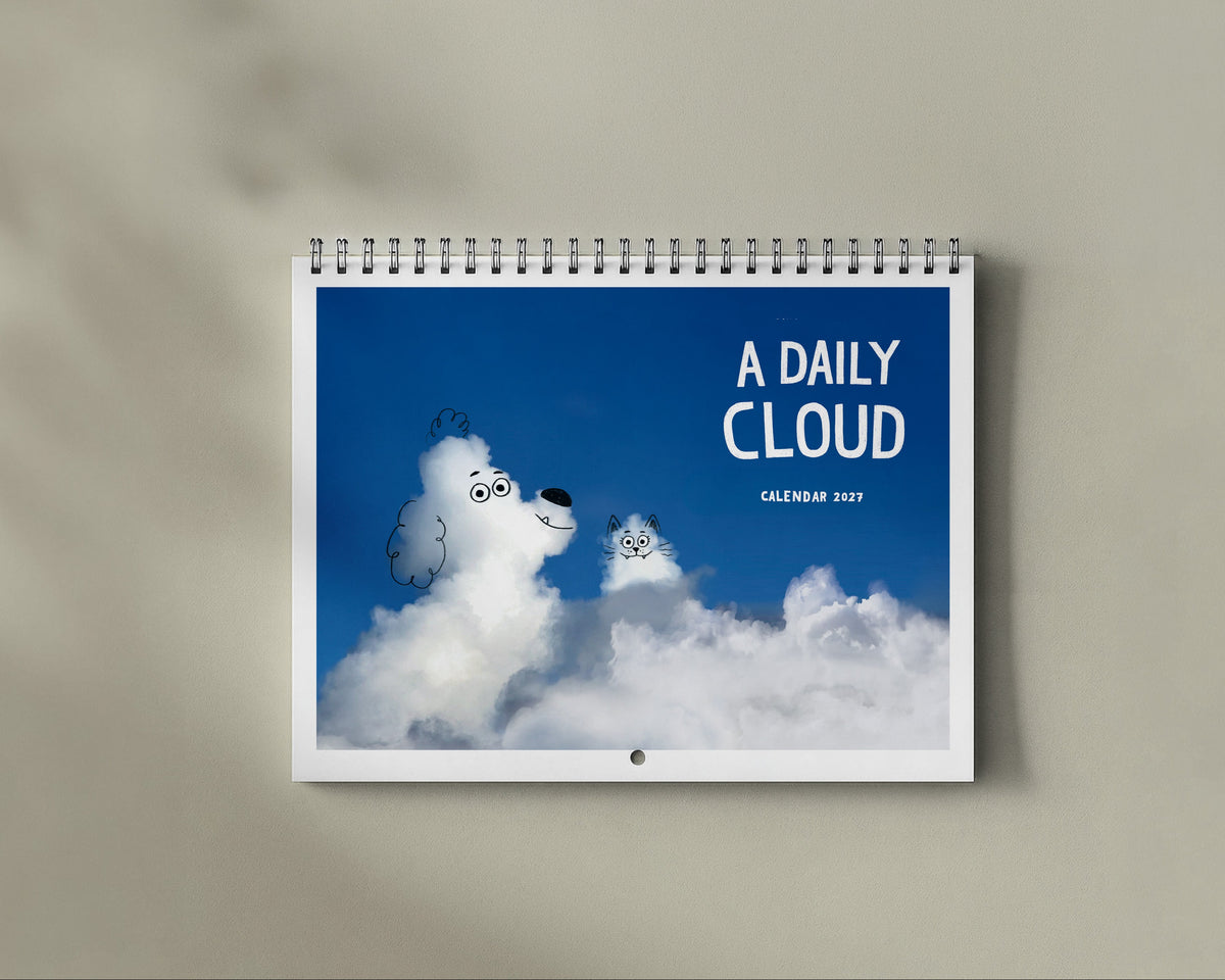 A spiral-bound desk calendar titled 'A DAILY CLOUD' hanging on a beige wall, featuring a blue sky and fluffy white clouds with cat and dog faces.