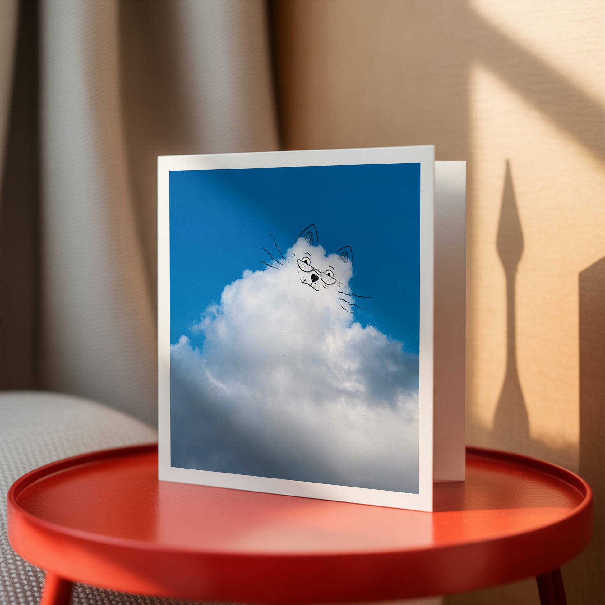 Card with a cat design on a cloud against a blue sky, placed on a red table.